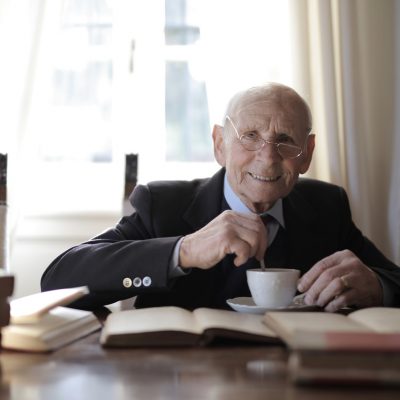 Elderly man wearing glasses and holding cup of tea